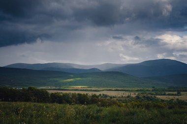 Fırtınadan önce dağların arasında resim gibi yeşil bir vadi. Kara bulutlar ve güneş ışınlarıyla dramatik bir gökyüzü. Arka planda bahar gökyüzü.