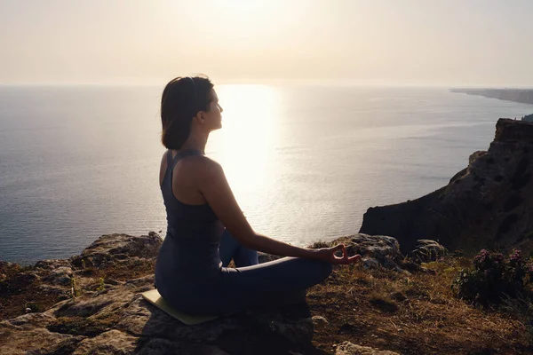 Gün batımı denizinde yoga yapan genç bir kadın. Nilüfer pozisyonunda meditasyon. Yoga silueti. Uyum ve meditasyon konsepti. Sağlıklı yaşam tarzı