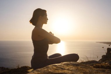 Gün batımı denizinde yoga yapan genç bir kadın. Nilüfer pozisyonunda meditasyon. Yoga silueti. Uyum ve meditasyon konsepti. Sağlıklı yaşam tarzı