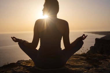 Gün batımı denizinde yoga yapan genç bir kadın. Nilüfer pozisyonunda meditasyon. Yoga silueti. Uyum ve meditasyon konsepti. Sağlıklı yaşam tarzı