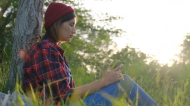 Günbatımı ormanında kendini izole eden güzel bir genç kız yalnızlığının tadını çıkarıyor. Sosyal uzaklık ve solo aktivite. Havalı kırmızı şapkalı Asyalı hipster portresi.