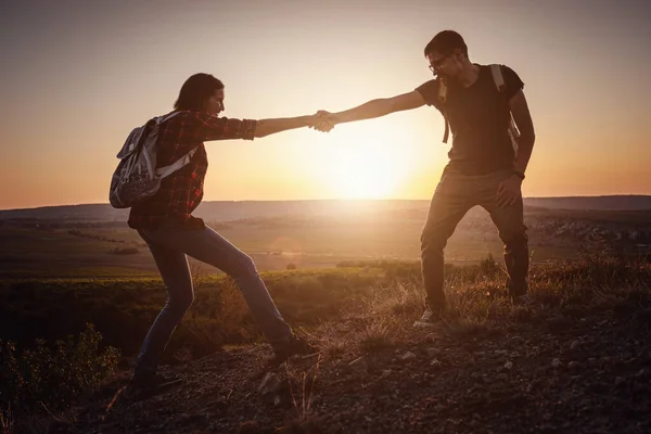 Silhouette in mountains, sunrise. Teamwork of man and woman hiker helping each other on top of mountain climbing team beautiful sunrise landscape. Two tourists with backpacks on mountain.