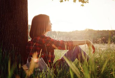 Genç hippi kız ormanda günbatımının tadını çıkarıyor. Sırt çantalı gezgin kadın. Doğanın günbatımının tadını çıkarıyorum. Gün doğumunda parkta dinleniyor. Trek konsepti