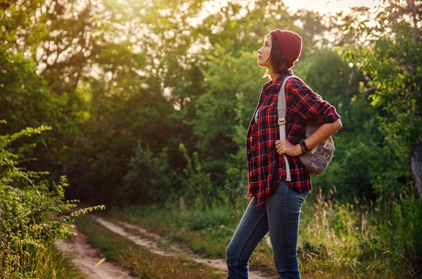 Genç hippi kız ormanda günbatımının tadını çıkarıyor. Sırt çantalı gezgin kadın. Doğanın günbatımının tadını çıkarıyorum. Gün doğumunda parkta dinleniyor. Trek konsepti