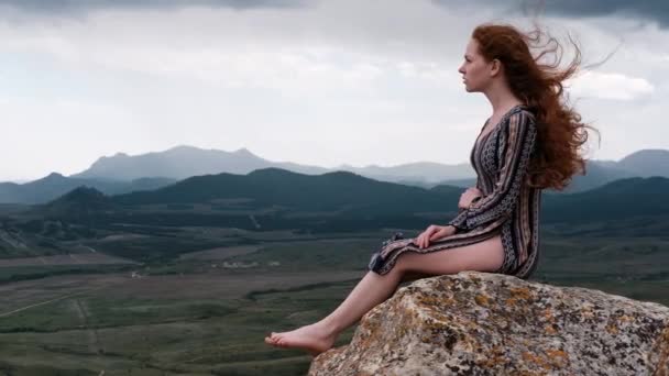 ジンジャーの女性は崖の上に座って 最後の光を見て 差し迫った嵐を見ています 風に髪を吹いて 女の子の山の風景を賞賛 クリミア クリミティネヴァ山 — ストック動画