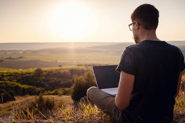 man with laptop sitting on the edge of a mountain with stunning views of the valley. Cellular network broaband coverage concept. 5G.