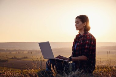 Dağın tepesinde bilgisayarıyla çalışan bir kız. Güneşin doğuşunda dağlarda dinlenip çalışmak.