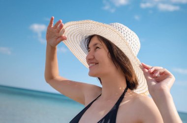 Plajda Şapka Giyen Güzel Genç Kadın. Yaz tatili, tatil, seyahat ve insanlar konsepti. Mayolu esmer kız sahilde yürüyor ve eğleniyor..