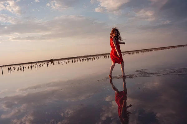 塩湖を歩いて絹のような赤いドレスを着たエレガントな女性 ロマンチックな気分だ 雲と空の空間の水の反射 休暇旅行シーン シバシュ湖 — ストック写真