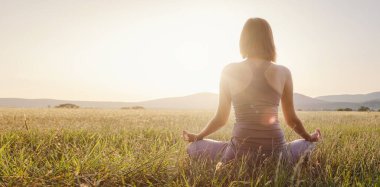 Kadın yoga yapıyor ve sahada lotus pozisyonunda meditasyon yapıyor. Sağlıklı yaşam tarzı ve yoga konsepti.
