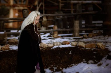 Kalenin zeminine karşı siyah pelerin giymiş güzel sarışın Viking. Güzel bir film seti. Eski bir Viking köyü.