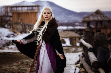 Kalenin zeminine karşı siyah pelerin giymiş güzel sarışın Viking. Güzel bir film seti. Eski bir Viking köyü.