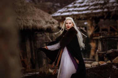 Kalenin zeminine karşı siyah pelerin giymiş güzel sarışın Viking. Güzel bir film seti. Eski bir Viking köyü.