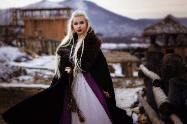Kalenin zeminine karşı siyah pelerin giymiş güzel sarışın Viking. Güzel bir film seti. Eski bir Viking köyü.