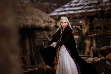 Kalenin zeminine karşı siyah pelerin giymiş güzel sarışın Viking. Güzel bir film seti. Eski bir Viking köyü.
