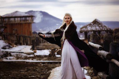 Kalenin zeminine karşı siyah pelerin giymiş güzel sarışın Viking. Güzel bir film seti. Eski bir Viking köyü.