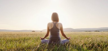 Kadın yoga yapıyor ve sahada lotus pozisyonunda meditasyon yapıyor. Sağlıklı yaşam tarzı ve yoga konsepti.