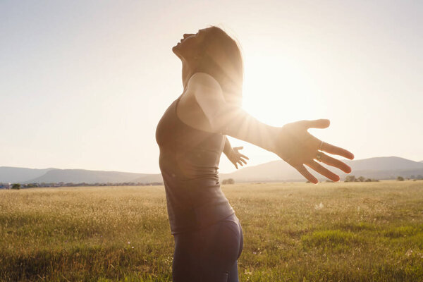 Young girl spreading hands with joy and inspiration facing the sun. She is enjoying serene nature workout vacation outdoors. asian beauty.