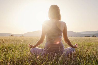 Kadın yoga yapıyor ve sahada lotus pozisyonunda meditasyon yapıyor. Sağlıklı yaşam tarzı ve yoga konsepti.