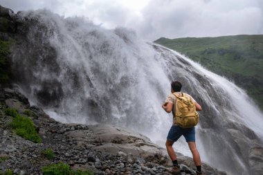 Şelale manzarası ve erkek gezgin şelale manzarasının keyfini çıkarıyor. Doğayla uyum içinde aktif tatiller. Yürüyüş ya da tırmanış için görüntü. Alibek Şelalesi, Kuzey Kafkasya, Dombai, Rusya.