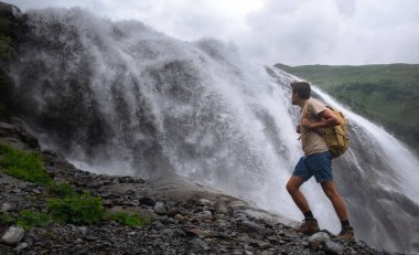 Şelale manzarası ve erkek gezgin şelale manzarasının keyfini çıkarıyor. Doğayla uyum içinde aktif tatiller. Yürüyüş ya da tırmanış için görüntü. Alibek Şelalesi, Kuzey Kafkasya, Dombai, Rusya.