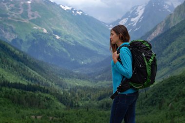 Dağın tepesinde, vadi manzarasının tadını çıkaran bir gezgin. Yolculuk konsepti, yazı için yer, atmosferik destansı an. Yürüyüş, yürüyüş ya da tırmanış için görüntü. Kuzey Kafkasya, Dombai, Rusya.