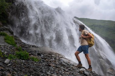 Şelale manzarası ve erkek gezgin şelale manzarasının keyfini çıkarıyor. Doğayla uyum içinde aktif tatiller. Yürüyüş ya da tırmanış için görüntü. Alibek Şelalesi, Kuzey Kafkasya, Dombai, Rusya.