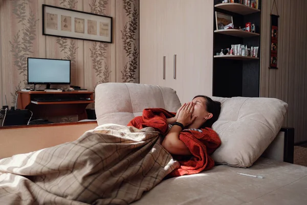 Sick and Flu Woman. Caught Cold. Woman feeling cold with blanket resting on the sofa at home