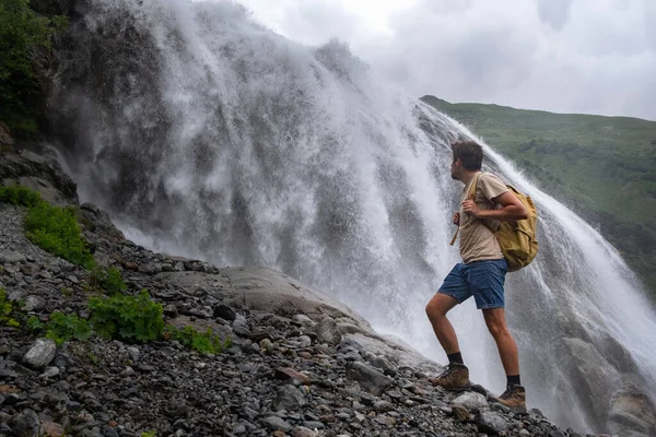 Waterfall Landscape and male Traveler enjoying waterfall view. active vacations into the wild harmony with nature. Image for hiking or climbing. Alibek Waterfall, North Caucasus, Dombai, Russia.