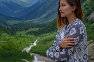Dağların tepesinde yürüyen şık bir bayan hippi. Güneşli dağları keşfeden mutlu genç bir kadın. Seyahat ve seyahat tutkusu konsepti. İnanılmaz atmosferik bir an. Kuzey Kafkasya, Dombai, Rusya.