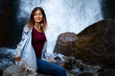 Şelalenin yanında oturan güzel kadın yürüyüşçü. Mutlu bir kadınla ekolojik konsept imajı. Şelale Shumka, Dombai, Karachay-Çerkessia, Rusya