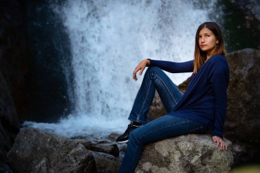 Şelalenin yanında oturan güzel kadın yürüyüşçü. Mutlu bir kadınla ekolojik konsept imajı. Karışık ırk Asyalı Kafkas gezgini. Şelale Shumka, Dombai, Karachay-Çerkessia, Rusya