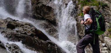 Sırt çantalı bir adam şelaleye bakıyor. Seyahat yaşam tarzı macera konsepti, doğayla uyum içinde aktif tatiller. Kuzey Kafkasya, Dombai, Rusya.