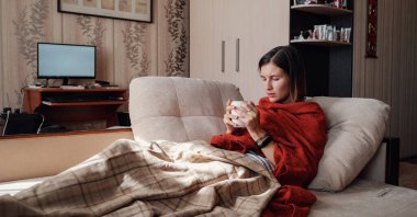 Hasta ve Grip Kadın. Soğuk algınlığına yakalandım. Kadın kendini üşümüş hissediyor. Evdeki kanepede dinleniyor.