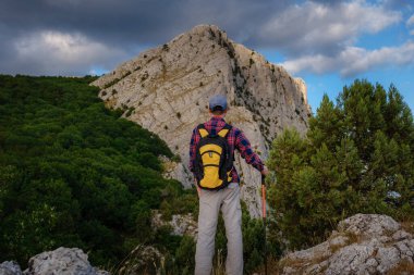 Yaz dağlarında, günbatımında uçurumun tepesinde duran ve doğanın tadını çıkaran genç adam..