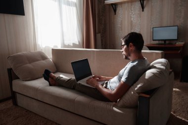 Uzaktan kumanda. Dizüstü bilgisayarda çalışan bir adam evdeki koltukta oturuyor. Metin için Boşluğu Kopyala. Serbest çalışan hipster, ortaklarıyla çalışır, çalışır ya da iletişim kurar.