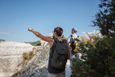 Sırt çantalı iki yürüyüşçü ve diğer tırmanma ekipmanları Rock 'ın tepesinde kalıyor. Adam eliyle güzergahı işaret ediyor. Plan, vizyon ve görev konsepti.