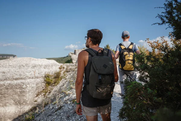 İki adam kayalık yamaçlarda yürüyüş çubuklarını kullanarak sırt çantalarını taşıyorlar. Dağlar Vadisi, insanların yanı sıra manzaralı. Doğaya yaz seyahati. Arka planda yürüyüşçü.