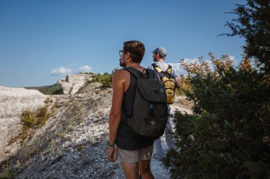 İki adam kayalık yamaçlarda yürüyüş çubuklarını kullanarak sırt çantalarını taşıyorlar. Dağlar Vadisi, insanların yanı sıra manzaralı. Doğaya yaz seyahati. Arka planda yürüyüşçü.