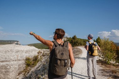 Sırt çantalı iki yürüyüşçü ve diğer tırmanma ekipmanları Rock 'ın tepesinde kalıyor. Adam eliyle güzergahı işaret ediyor. Plan, vizyon ve görev konsepti.