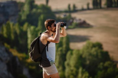 Tepedeki dürbüne bakan adam. Sırt çantalı bir adam. Vadi manzarasında yürüyüş yapan genç beyaz bir adam.