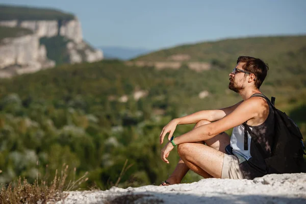 年轻的男性徒步旅行者带着背包在夏日平静的日落时在山顶上放松 度假的风景 累了的旅行者在山上休息 — 图库照片