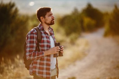 Tepedeki dürbüne bakan adam. Sırt çantalı bir adam. Vadi manzarasında yürüyüş yapan genç beyaz bir adam.