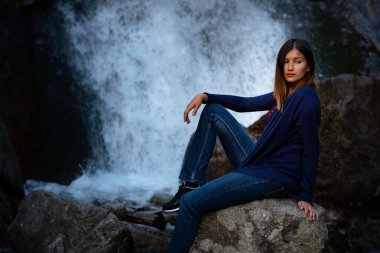 Şelalenin yanında oturan güzel kadın yürüyüşçü. Mutlu bir kadınla ekolojik konsept imajı. Karışık ırk Asyalı Kafkas gezgini. Şelale Shumka, Dombai, Karachay-Çerkessia, Rusya