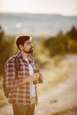 Tepedeki dürbüne bakan adam. Sırt çantalı bir adam. Vadi manzarasında yürüyüş yapan genç beyaz bir adam.