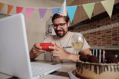 Karantina zamanında doğum gününü kutlayan bir adam. Coronavirus salgını 2020. Adam kutuyu açıyor ve hediyeyle çok mutlu oluyor. Arkadaşlarla uzaktan iletişim kurmak.