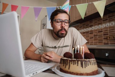 Karantina zamanında doğum gününü kutlayan bir adam. Adam doğum gününü kutluyor, pastadaki mumu söndürüyor ve video görüşmesi yapıyor. Coronavirüs salgını 2020.