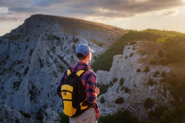 Maceracı adam dağın tepesinde ve canlı bir günbatımında güzel manzaranın tadını çıkarıyor. Başarı, kazanan, lider konsepti ve fikri