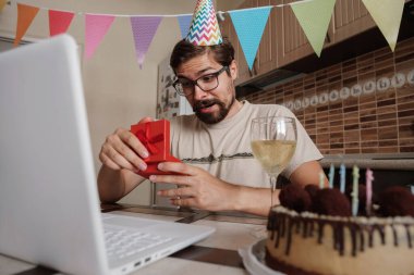 Karantina zamanında doğum gününü kutlayan bir adam. Coronavirus salgını 2020. Adam kutuyu açıyor ve hediyeyle çok mutlu oluyor. Arkadaşlarla uzaktan iletişim kurmak.