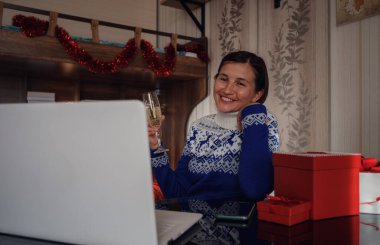 Noel çevrimiçi tebrikler. Mavi kazaklı gülümseyen Asyalı kadın bilgisayar kullanarak ailelerini ve arkadaşlarını arıyor. Duygusal yüz..
